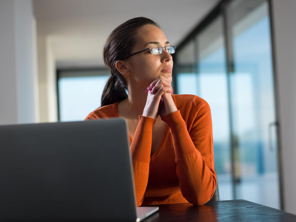 young woman looking out the window with laptop on the table