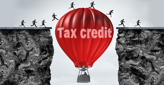 image of people walking on a hot air balloon that is placed in the middle of two cliffs. the red hot air balloon has "tax credit" written on it.