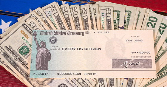 $20 bills spreadout on a table with a government issued check on top for the amount of $1,400 directed to "every US citizen"