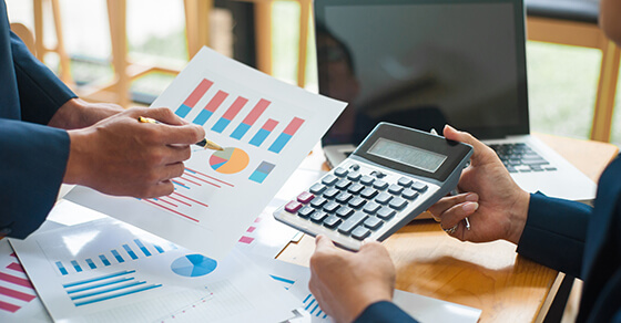 calculator and papers with graphs on a desk with two people holding papers