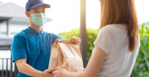 delivery person handing a bag to someone else. Delivery person has a mask on.