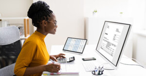 woman in front of a computer looking at the monitor with her fingers on a calculator