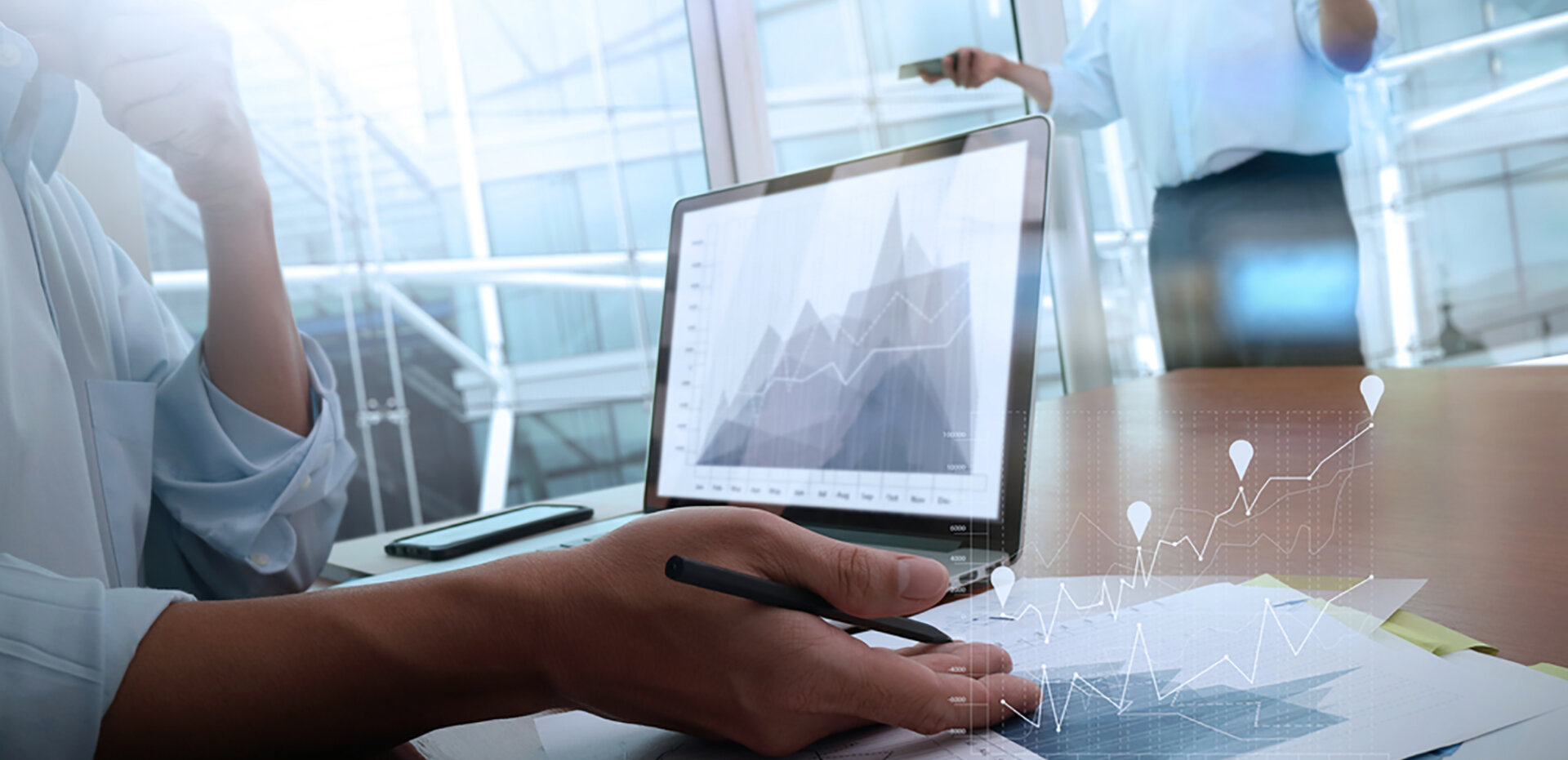 business-documents-on-office-table-with-smart-phone-and-laptop-computer-and-graph-business-with-social-network-diagram-and-two-colleagues-discussing-data-in-the-background