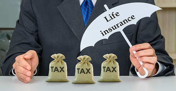 An individual holding an umbrella over three little bags of money. The umbrella says "Life Insurance"