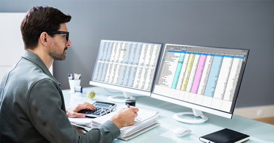 individual looks at two open computer screens on his desk.