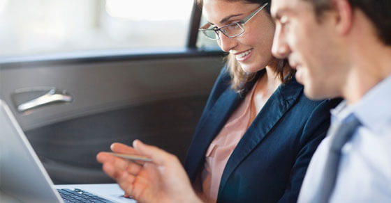 Two people in a car looking the screen of an open laptop.