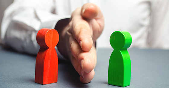 image of two colorful wooden images depicting people (one is red, one is green) with a hand down the middle to separate them from coming together.