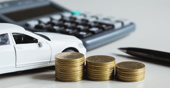 calculator, mini model car and coins on a table.
