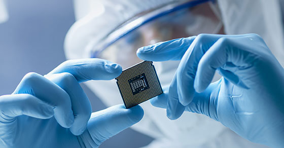 person covered in PPE holding a microchip and studying it.