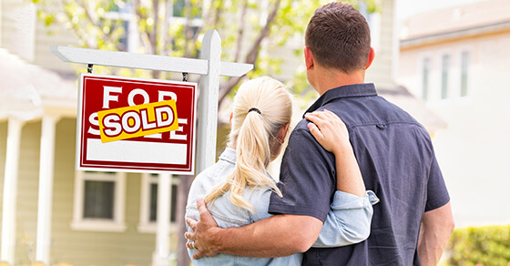 people in front of a "sold" sign, embracing.