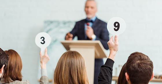 back view of buyers showing auction paddles with numbers nine and three to auctioneer during auction