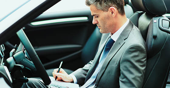 Businessman sitting in his car, he is planning and scheduling meetings on his organizer and using apps on his smartphone