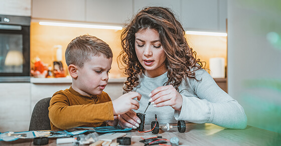 parent and child working on a project at a kitchen table. 