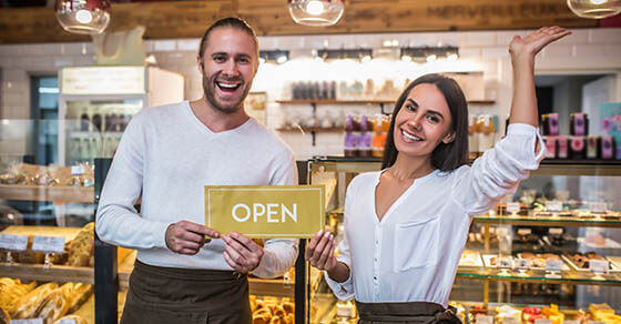 Smiling broadly. Cheerful good-looking husband and wife smiling broadly while opening their own bakery