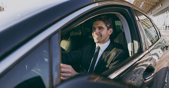 Side profile view smiling young driver smiling businessman man 20s wear black dinner suit driving car taxi hold steering wheel look camera Vehicle transport traffic lifestyle business trip concept