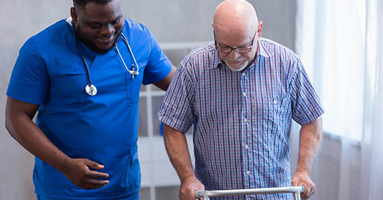 Caregiver is teaching old man to walk with walker. Professional nurse and patient in a nursing home. Assistance, rehabilitation and health.