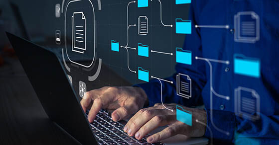 Document Management System (DMS) being setup by IT consultant working on laptop computer in office. Software for archiving, searching and managing corporate files and information. Business processes