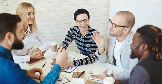 Portrait of bearded businessman in eyeglasses expressing his point of view on topical issue while sitting in meeting room with multiethnic group of coworkers