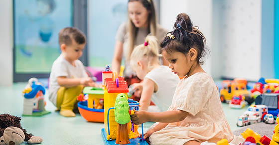 Nursery school. Toddlers and their teacher playing with colorful plastic playhouses, cars and boats. Imagination, creativity, fine motor and gross motor skills development. High quality photo