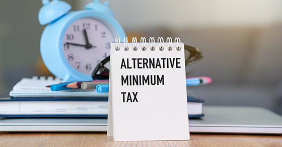 notebook with "alternative minimum tax" written on it, standing in front of books and a clock