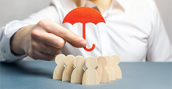 image of a person holding an umbrella over small wooden blocks shaped like people, huddled under the umbrella.